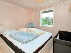 A single bed with a mattress, pillows, and a blanket in a room with wooden walls and a window.
