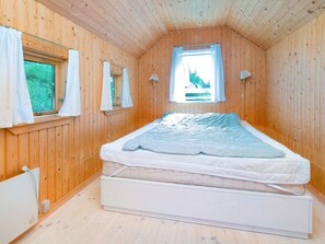 Una habitació petita amb panells de fusta, un llit individual, dues finestres amb cortines i un sostre inclinat.
