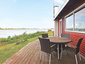 A wooden deck with a table and chairs overlooking a body of water. - 4 Person Holiday Home in Martofte (Martofte)