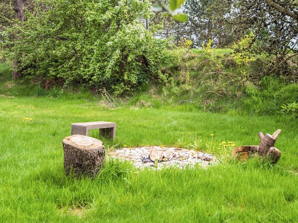 A natural outdoor setting with a stone bench, a tree stump, and a small wooden structure in a grassy area.
