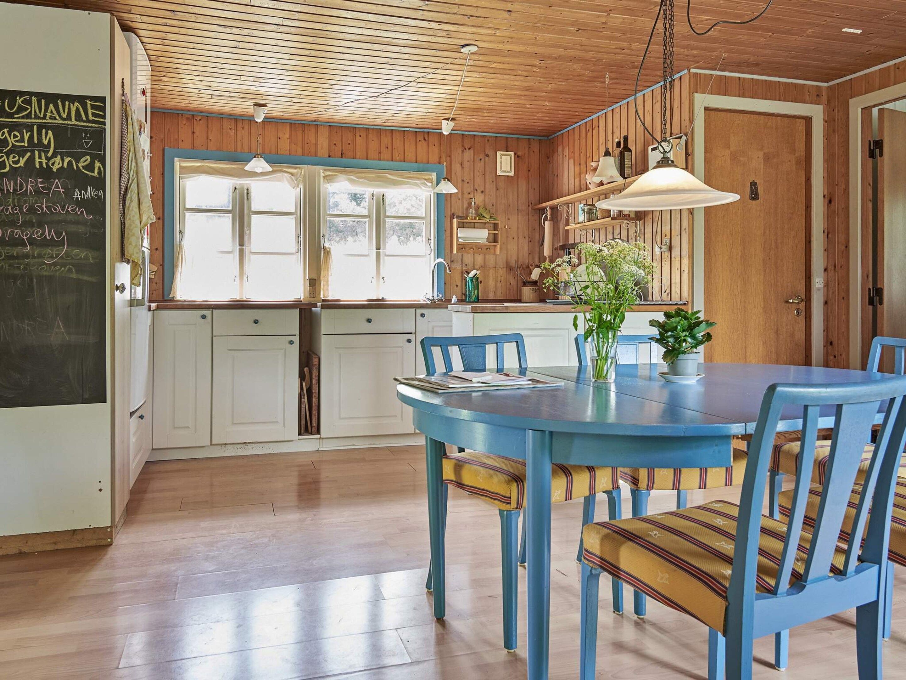 A kitchen with wooden cabinets, a blue table with chairs, and a chalkboard with writing.
