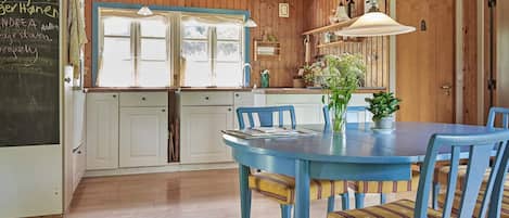 A kitchen with wooden cabinets, a blue table with chairs, and a chalkboard with writing.