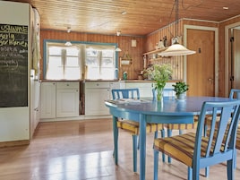 Et køkken med træskabe, et blåt bord med stole og en tavle med skrift.