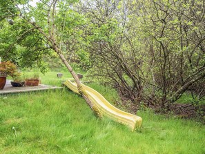 A yellow slide in a grassy area with trees and potted plants.