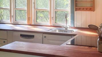 A kitchen with a sink, wooden countertop, and a window with a view of greenery.