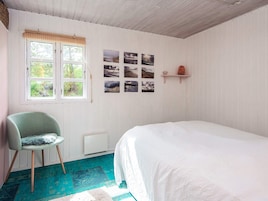 Un dormitorio con una cama, una silla, un ventanal con persianas y una pared decorada con varias fotografías.