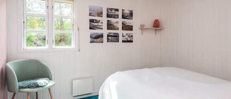 Une chambre à coucher avec un lit, une chaise, une fenêtre et des tableaux accrochés au mur.