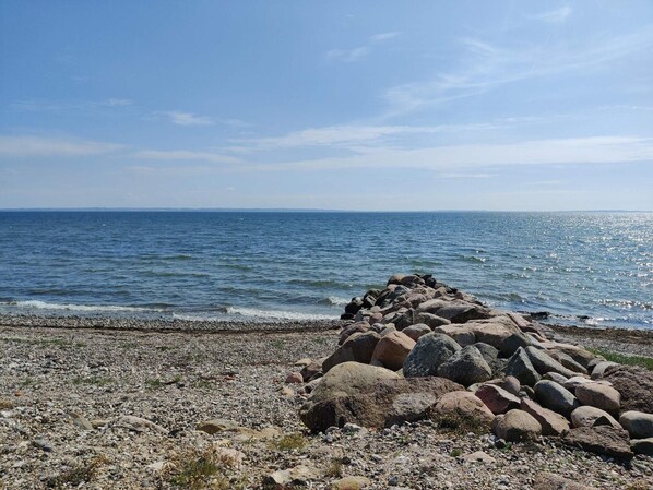 A rocky shoreline with a pile of large rocks in the foreground and calm sea under a clear sky.