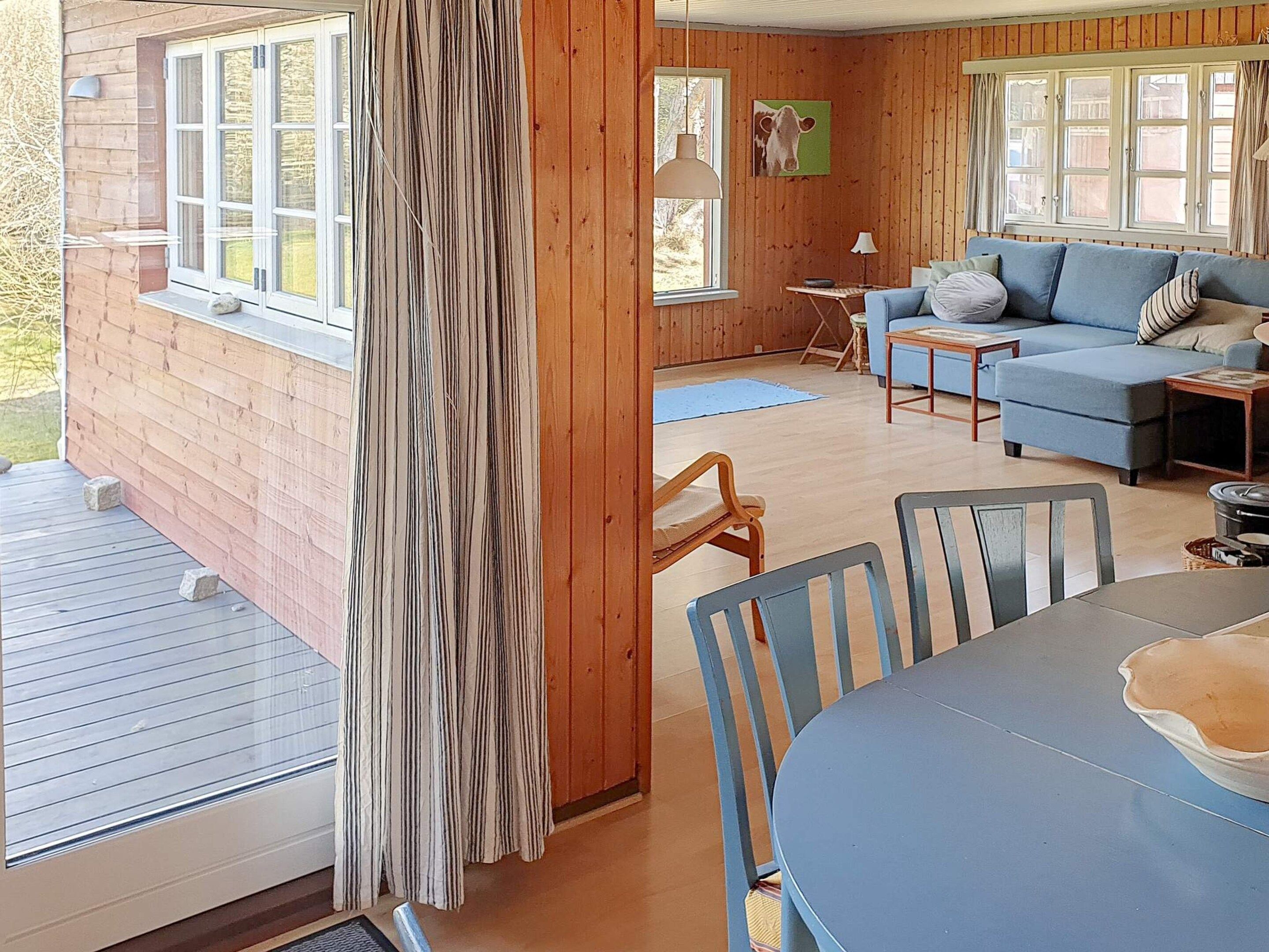 A wooden cabin interior with a dining area, a sofa, and a window with curtains.