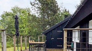 Un terrazzo in legno con tavolo e sedie, un oggetto blu e un edificio nero con una porta.