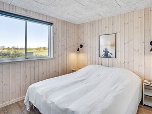 A bedroom with a large bed, a window, a wall-mounted lamp, and a framed picture.
