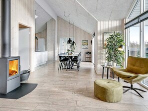 A modern interior with a wood-burning stove, a dining area, and a large window.