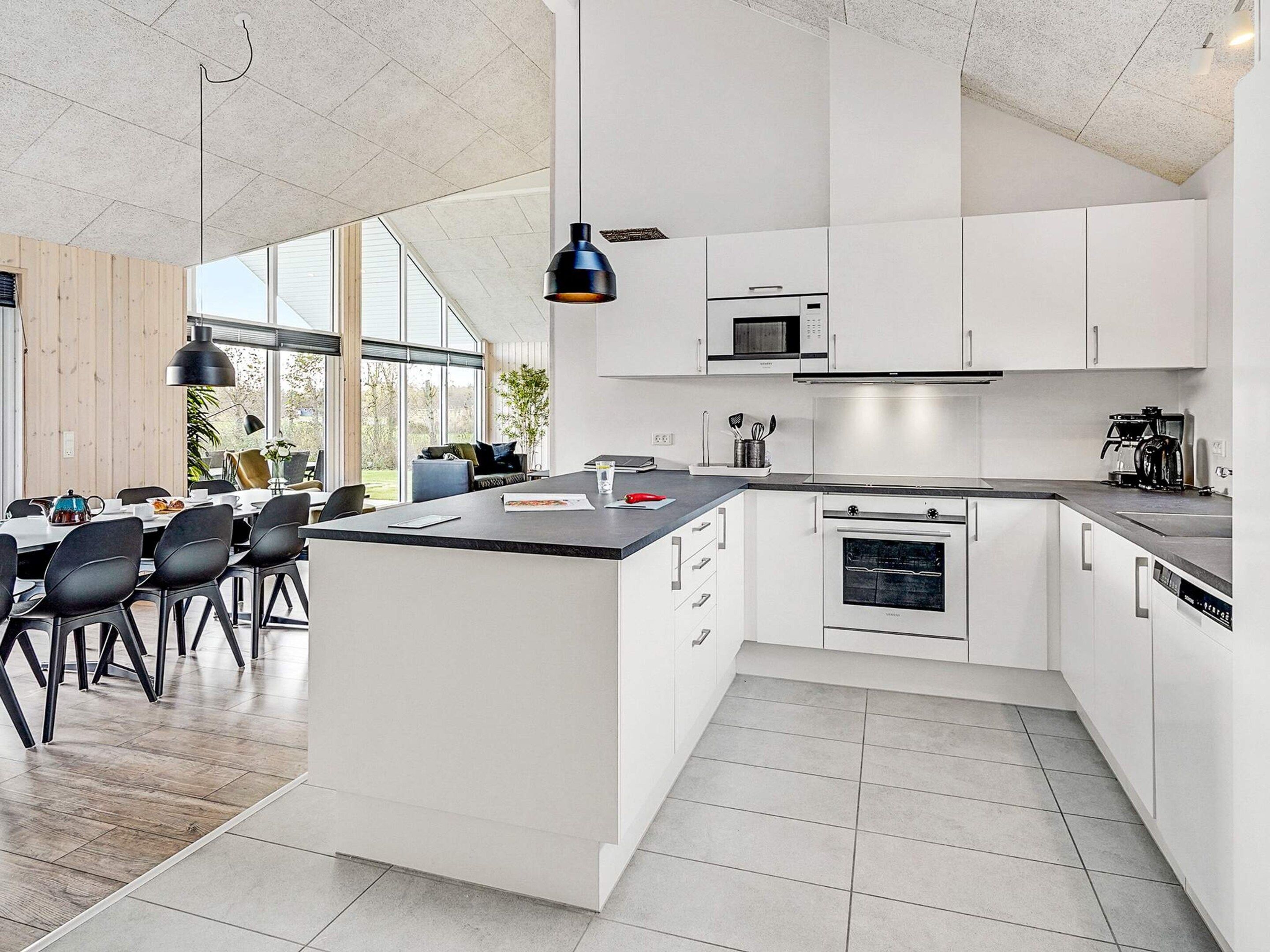 A modern kitchen with white cabinetry, a central island, and a dining area with black chairs.