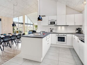A modern kitchen with white cabinetry, a central island, and a dining area with black chairs. - 5 Star Holiday Home in Idestrup (Idestrup)