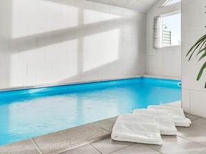 A swimming pool with clear blue water, surrounded by white tiled walls and a window with a view.