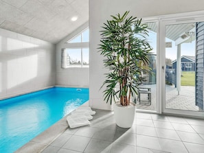 En swimmingpool med ett kaklat golv, en krukväxt och en skjutdörr i glas som leder ut till ett utomhusområde.