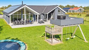 Una casa con un'ampia terrazza, una piscina e una struttura in legno separata con altalena.