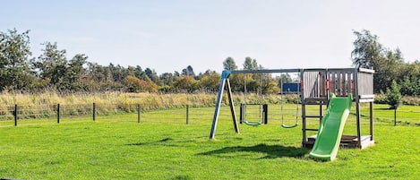A playground with swings and a slide in a grassy area.