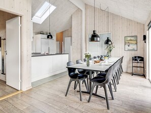 A modern kitchen with white cabinets, a dining area with a long table and chairs, and a wooden floor. - 5 Star Holiday Home in Idestrup (Idestrup)