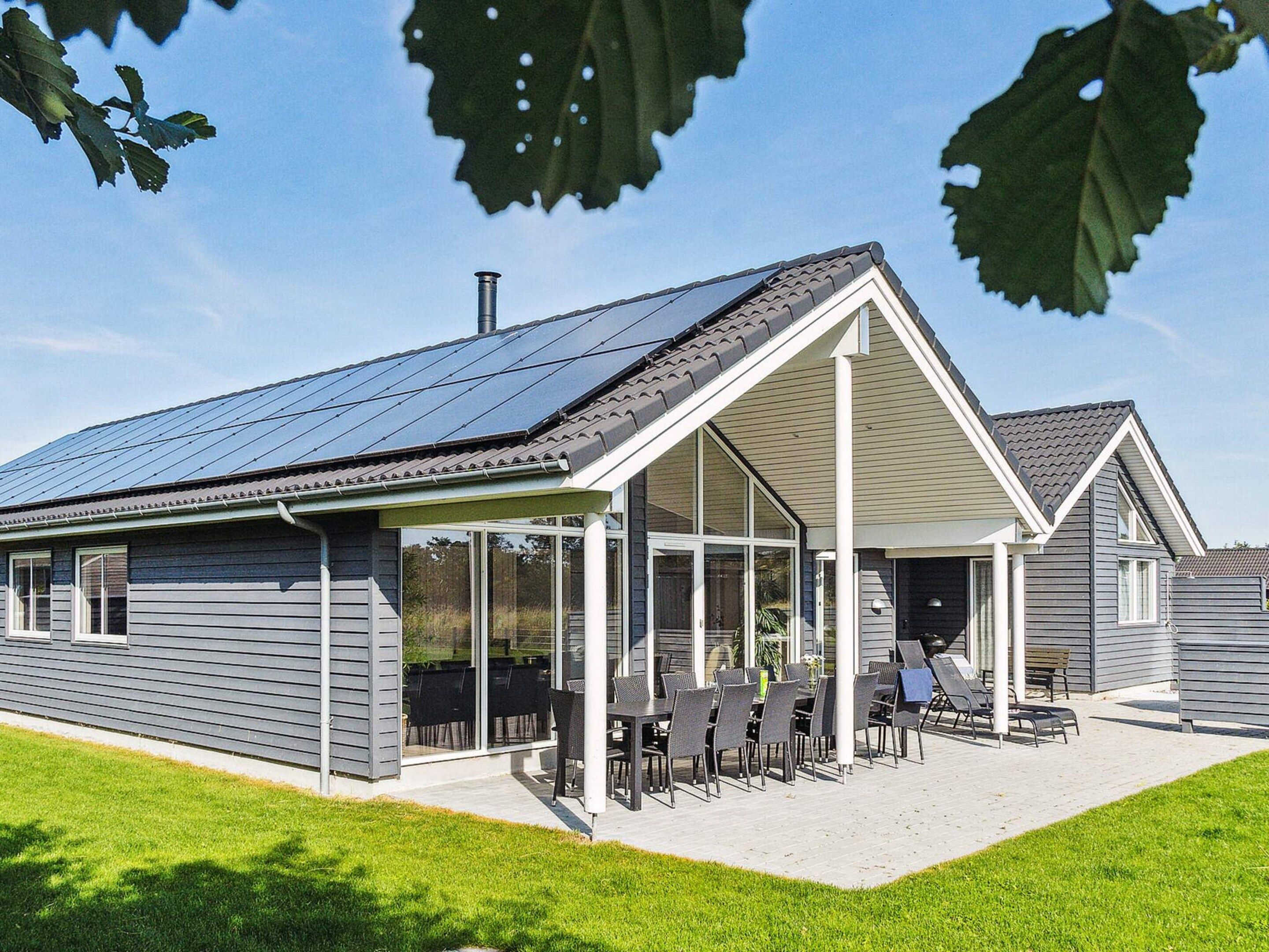 Une maison moderne dotée d’un patio couvert, de panneaux solaires et d’une pelouse bien entretenue.
