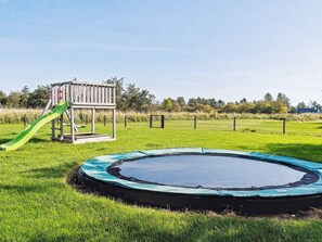 A playground with a slide and a trampoline in a grassy field.