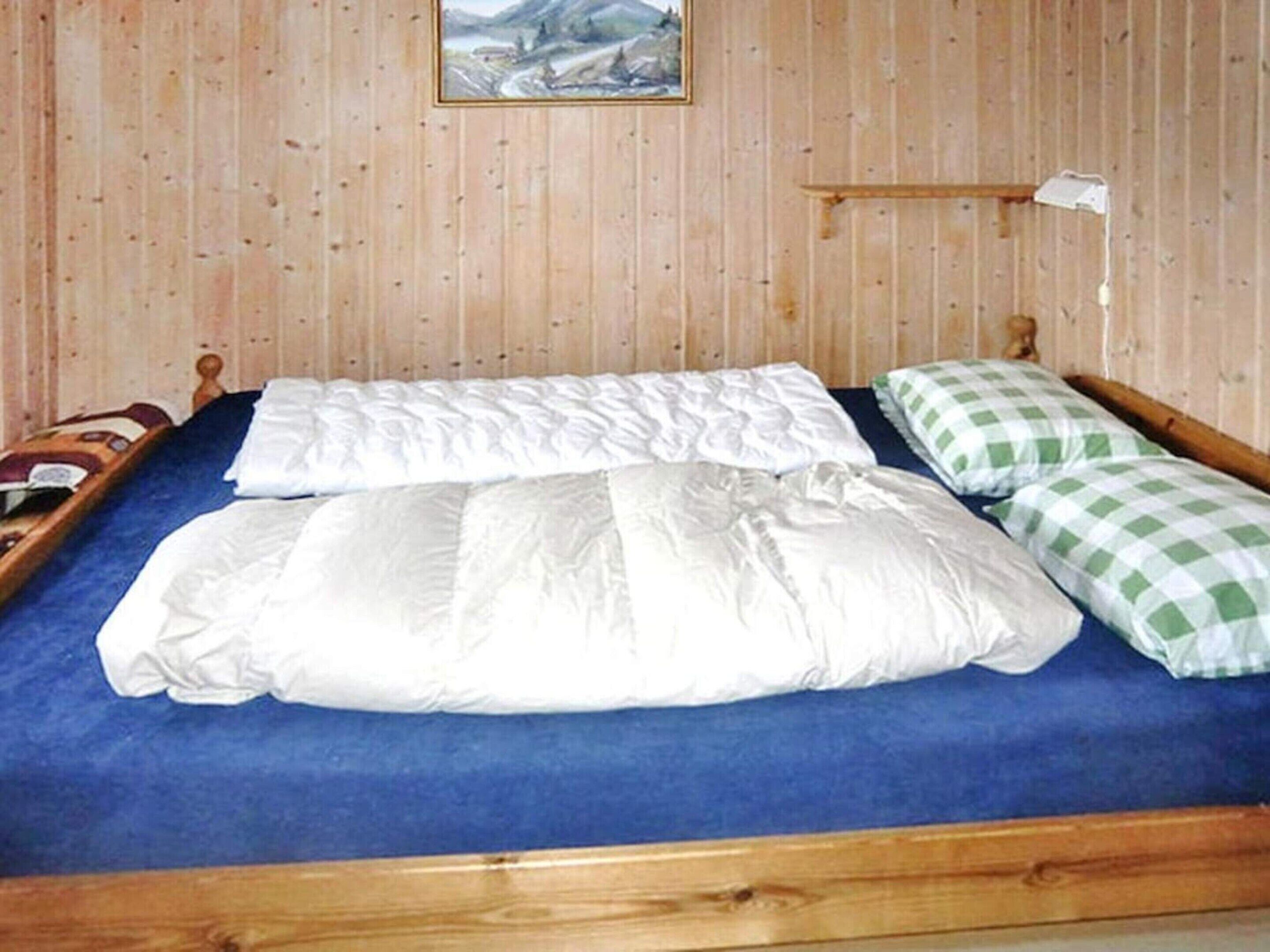 Una cama de madera con un colchón azul, almohadas a cuadros blancos y verdes, y cabecera de madera.