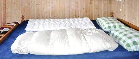 Una cama de madera con un colchón azul, almohadas a cuadros blancos y verdes, y cabecera de madera.
