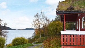 A cabin with a red exterior and a thatched roof, situated by a lake with a gravel path leading to it. - 6 Person Holiday Home in Vatne (Ålesund)