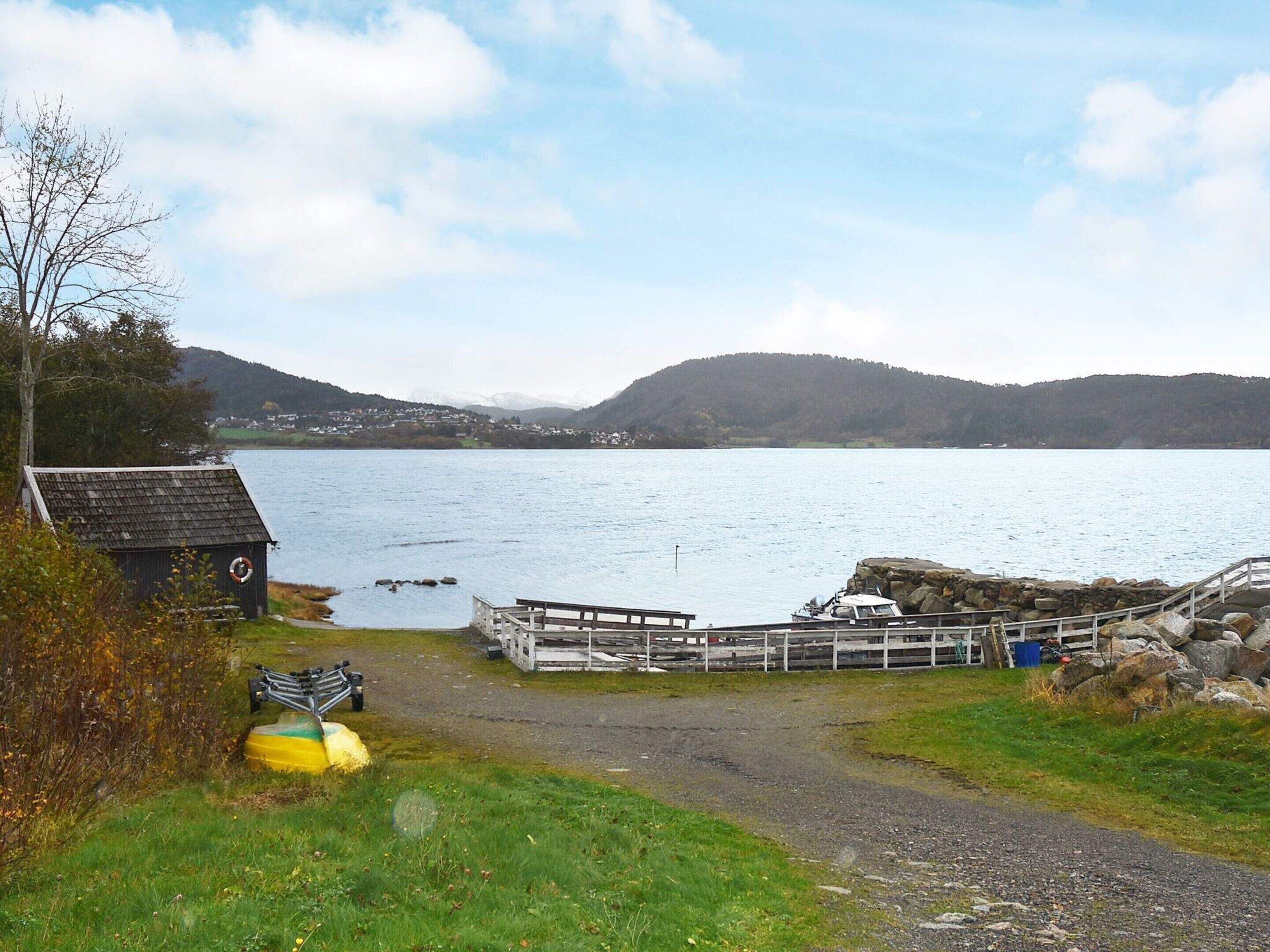 A lakeside dock with a small building and a wooden walkway leading to a boat.