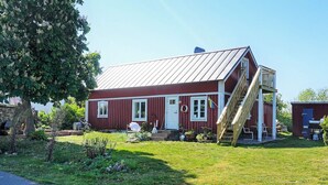 A red wooden house with a metal roof, a wooden staircase, and a small garden area. - 6 Person Holiday Home in Solvesborg (Sölvesborg)
