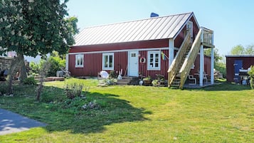 A red wooden house with a metal roof, a wooden staircase, and a small garden area.