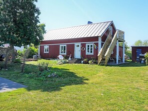 A red wooden house with a metal roof, a wooden staircase, and a small garden area. - 6 Person Holiday Home in Solvesborg (Sölvesborg)