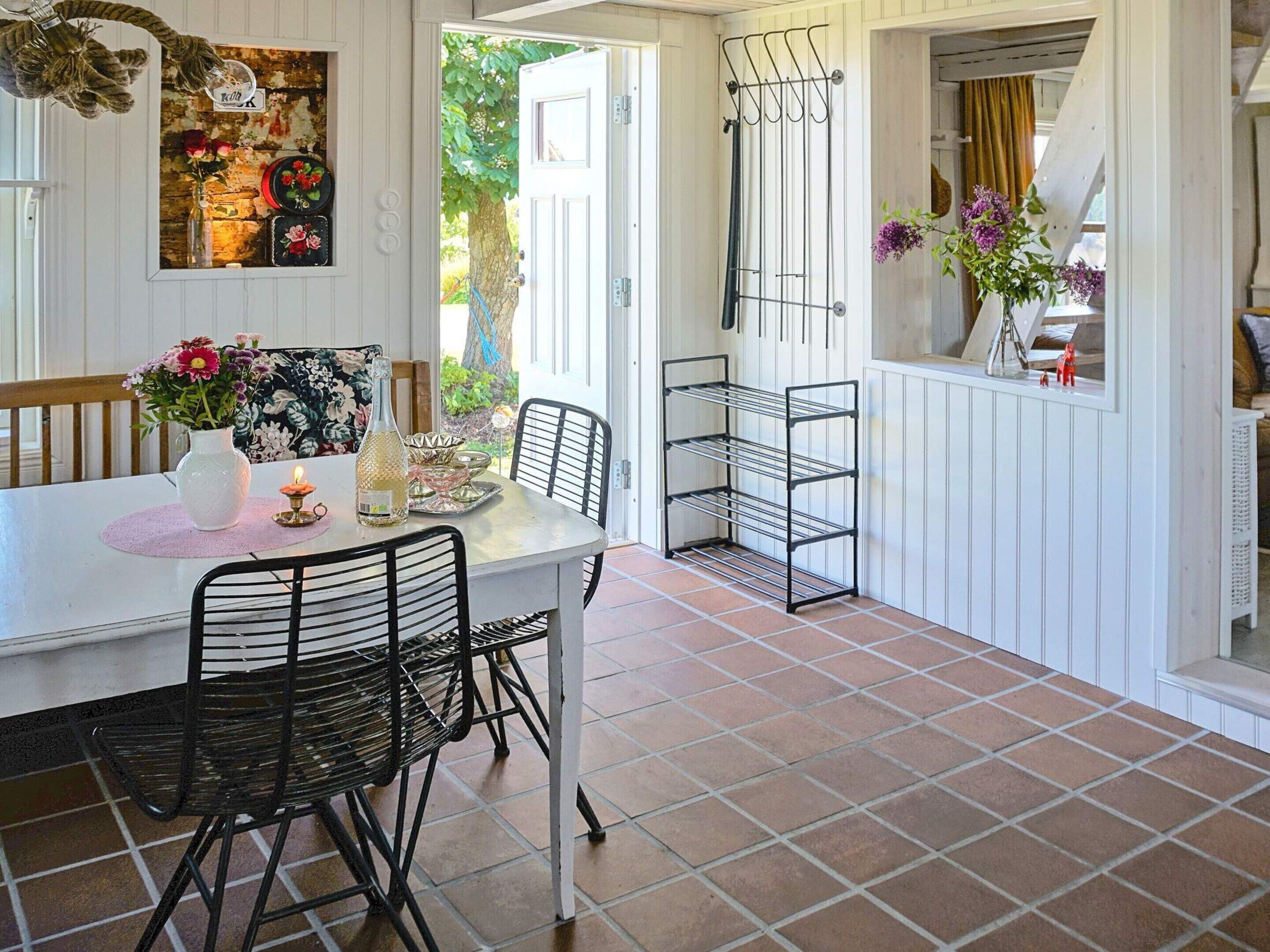 Un comedor con una mesa blanca, sillas negras, un florero con flores y un escurreplatos de metal.