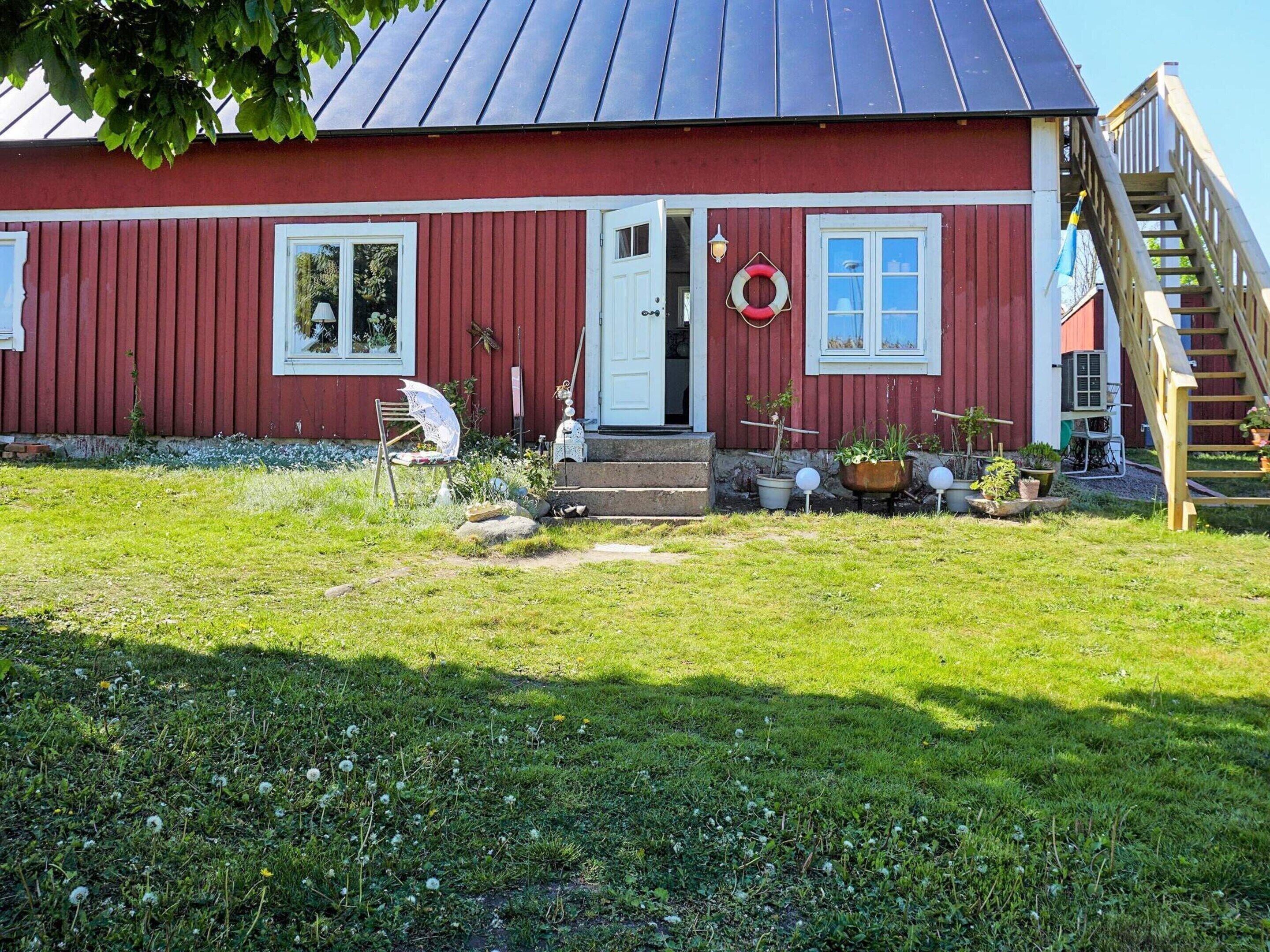 Una casa de madera roja con techo de metal, una puerta principal y un pequeño porche con plantas en macetas.