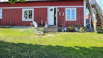 Una casa de madera roja con techo de metal, una puerta principal y un pequeño porche con plantas en macetas.