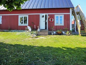 A red wooden house with a metal roof, a front door, and a small porch area with potted plants.