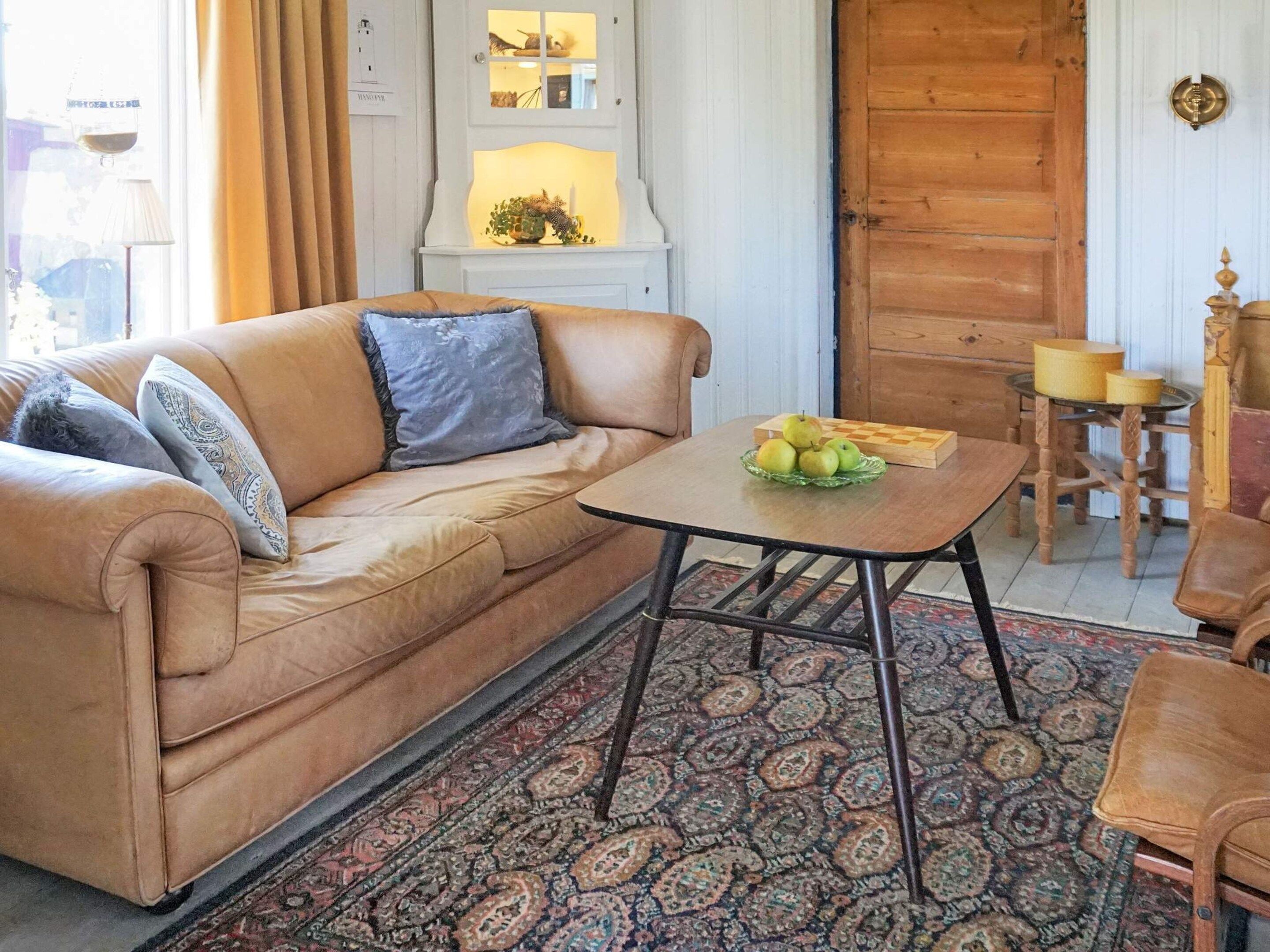 A cozy living room with a brown leather sofa, a patterned rug, and a table with a fruit bowl.