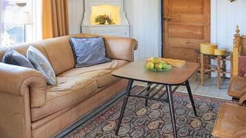 A cozy living room with a brown leather sofa, a patterned rug, and a table with a fruit bowl.