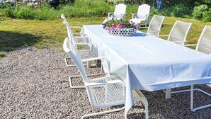 An outdoor dining area with a table set for six, surrounded by white chairs, a flower basket, and a flag. - 6 Person Holiday Home in Solvesborg (Sölvesborg)
