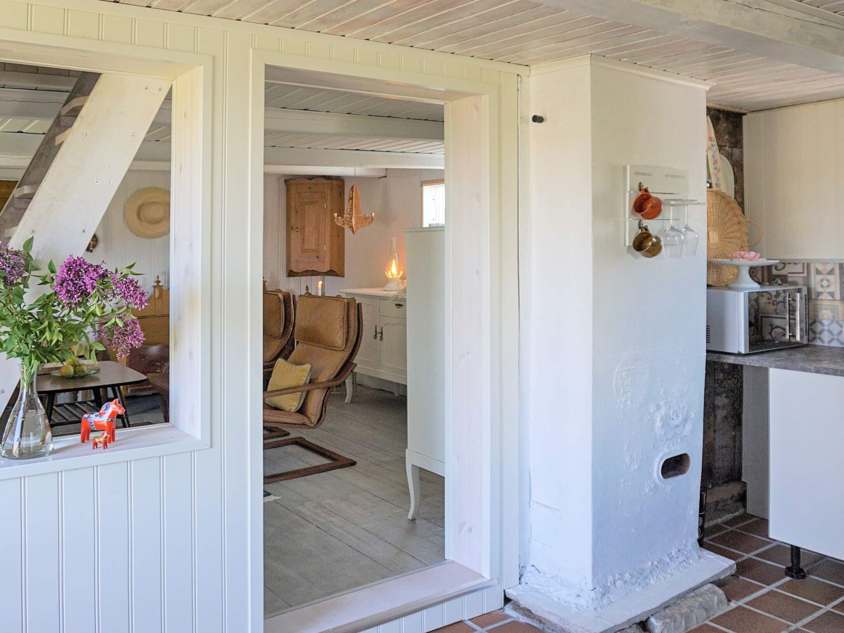 A room with a white door leading to a kitchen area, a dining table with chairs, and a vase with flowers on the windowsill.