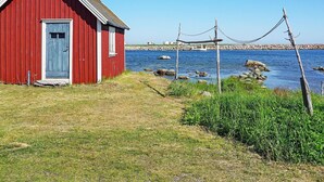 A red wooden building with a door and window, situated by a body of water with rocks and vegetation. - 6 Person Holiday Home in Solvesborg (Sölvesborg)