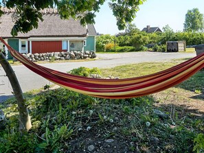 A hammock tied between two trees in a residential area with a house and a stone wall in the background. - 6 Person Holiday Home in Solvesborg (Sölvesborg)