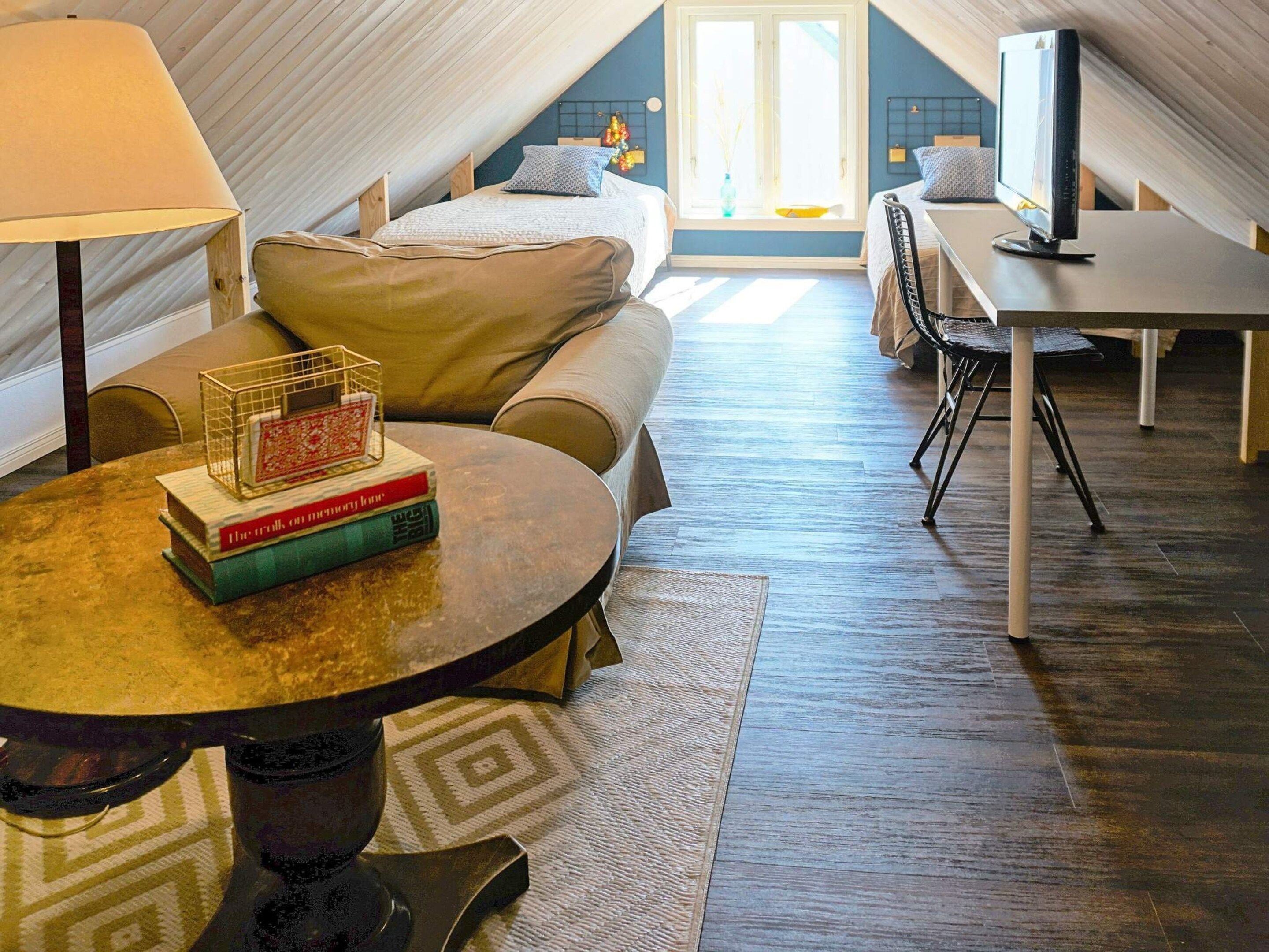 A cozy attic bedroom with a bed, a desk, and a table with books.