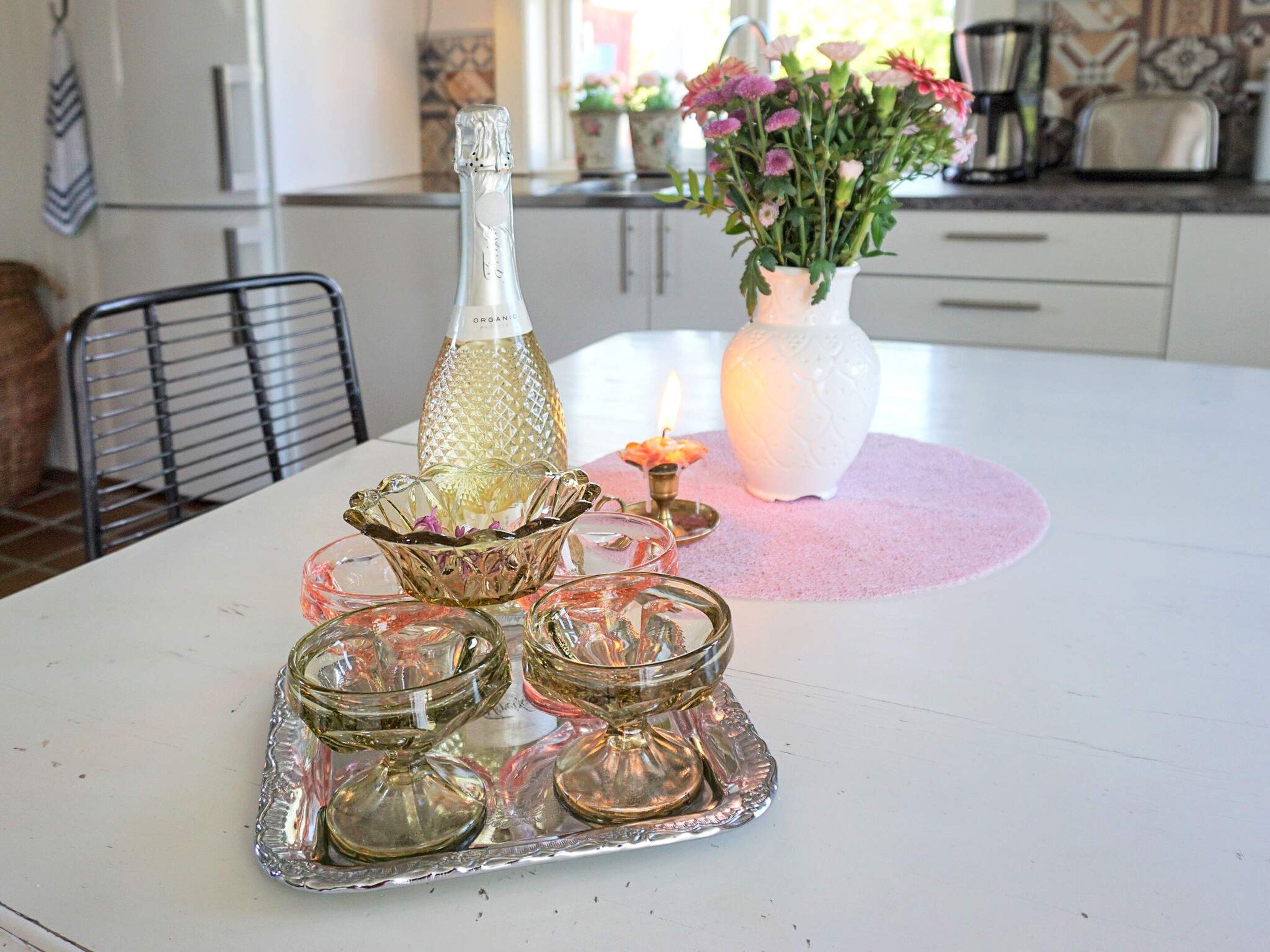 A dining table with a bottle, a vase with flowers, and a tray with glassware.