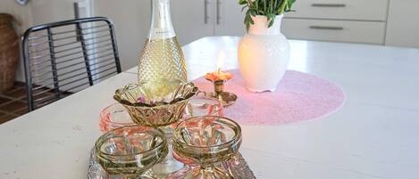 A dining table with a bottle, a vase with flowers, and a tray with glassware.
