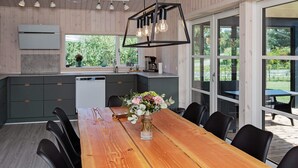 A modern kitchen with wooden cabinets, a built-in dishwasher, and a large dining table with chairs. - 5 Star Holiday Home in Vaeggerlose (Vaeggerlose)