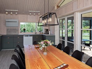 A modern kitchen with wooden cabinets, a built-in dishwasher, and a large dining table with chairs. - 5 Star Holiday Home in Vaeggerlose (Vaeggerlose)