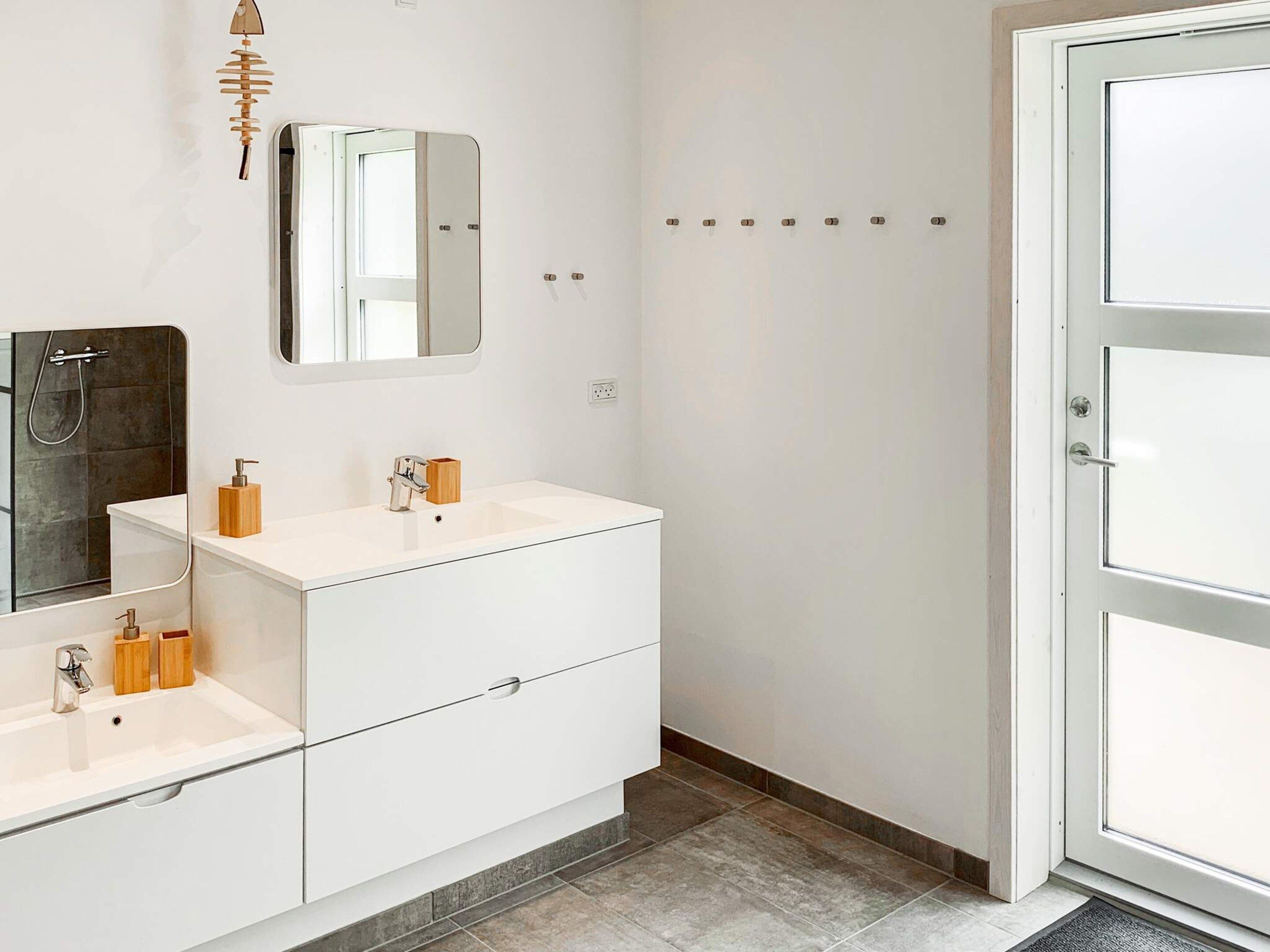 Une salle de bain moderne avec un meuble-lavabo blanc, un miroir, une douche et une porte dotée d’une poignée.