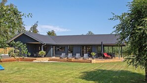 A modern house with a covered patio, a lawn, and a wooden deck. - 5 Star Holiday Home in Vaeggerlose (Vaeggerlose)