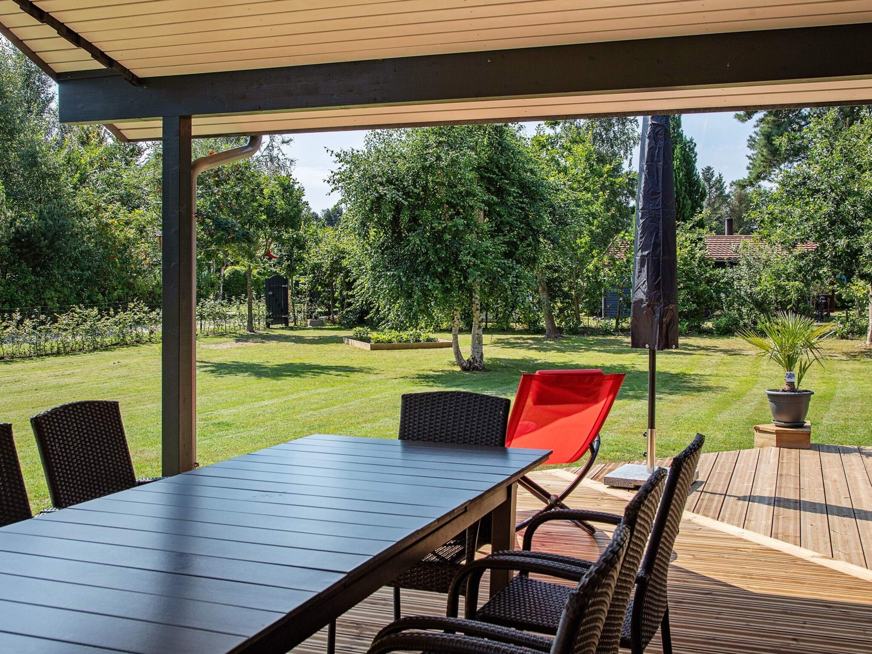 An outdoor patio with a table and chairs, surrounded by a wooden deck and a garden.